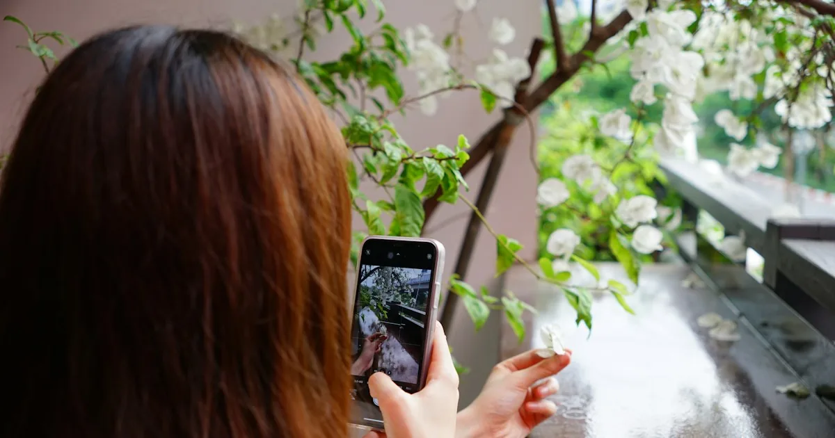 Mujer fotografiando flores con su móvil en una terraza