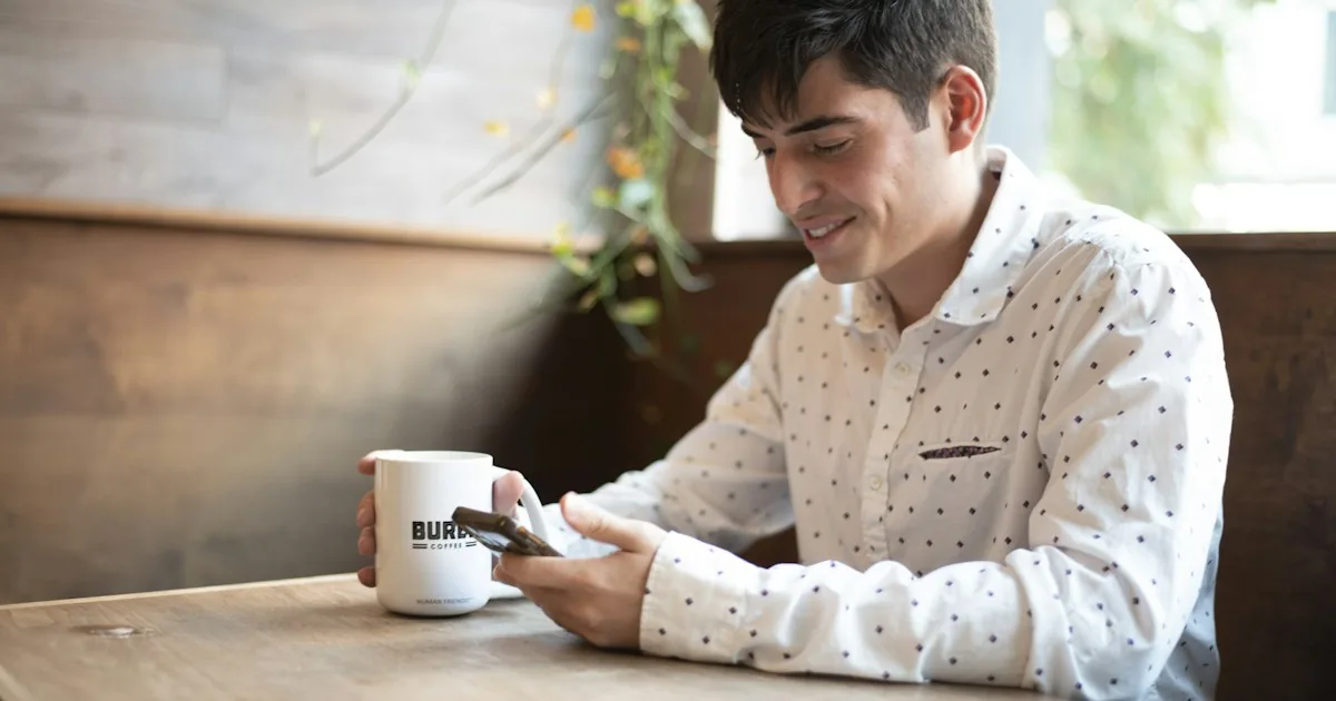 Hombre sonriendo mientras lee en el móvil en una cafetería