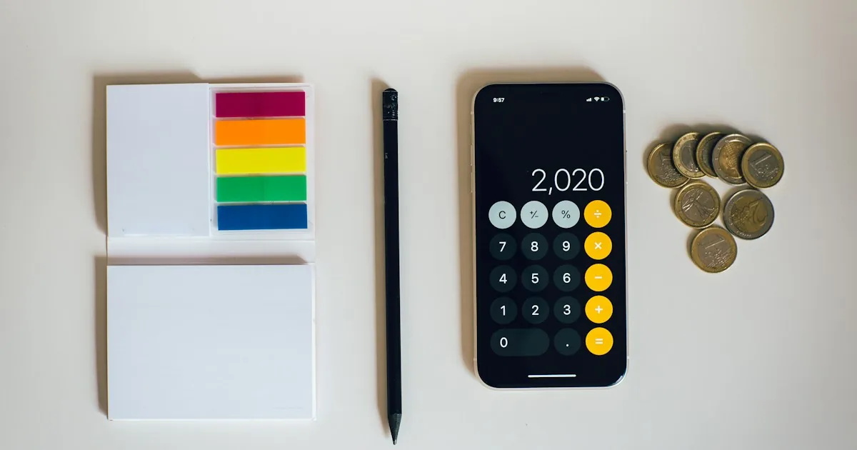 Móvil con la calculadora abierta junto a monedas, libretas y un bolígrafo