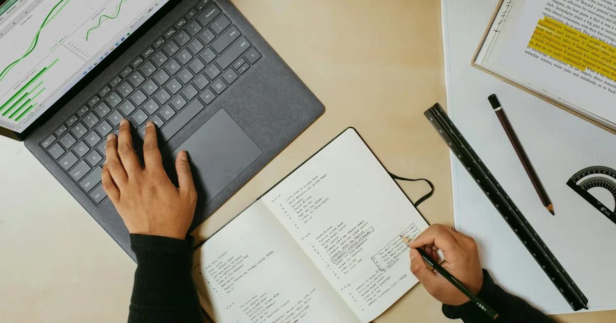 Persona comparando notas en una libreta mientras trabaja con un portátil